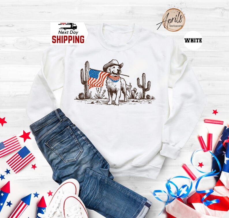 Pu&ograve; includere: Felpa bianca con grafica di un cane con cappello da cowboy e bandiera americana. Il cane &egrave; davanti ai cactus. Le parole "Next Day Shipping" sono stampate in alto a sinistra.