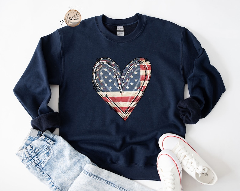 Puede incluir: Una sudadera azul marino con un dise&ntilde;o de coraz&oacute;n de bandera estadounidense desgastado.