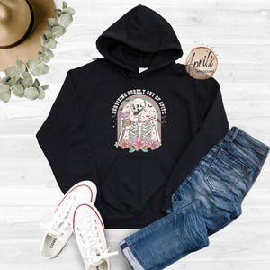 May include: Black hoodie featuring a graphic of a skeleton holding a drink with the text "Surviving purely out of spite".