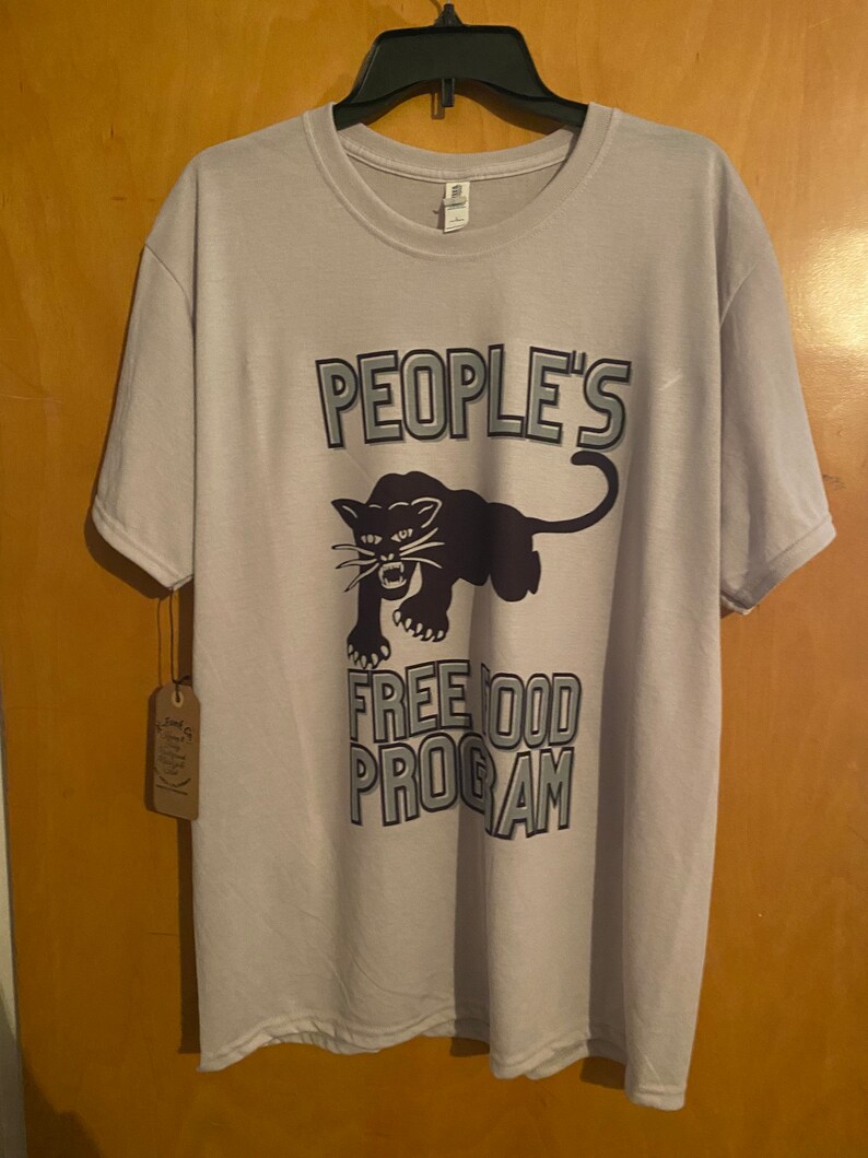 Pode incluir: Uma camiseta cinza claro com um gr&aacute;fico de pantera negra e o texto "PEOPLE'S FREE FOOD PROGRAM" em uma fonte em negrito e com contorno.