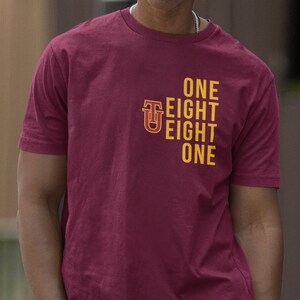 May include: A maroon t-shirt with a gold graphic design that reads "ONE EIGHT EIGHT ONE" with a stylized "U" in the center.