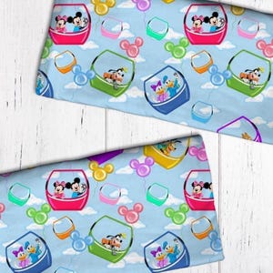 May include: Light blue fabric featuring a repeating pattern of Disney characters in colorful gondolas and Mickey Mouse-shaped balloons against a sky with white clouds. Characters include Mickey, Minnie, Donald, Daisy, and Goofy.