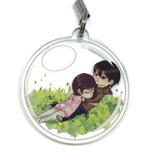 May include: A clear round keychain with a printed image of a couple lying on a bed of green grass. The couple is drawn in a cartoon style and the woman is wearing a pink shirt and the man is wearing a brown shirt.