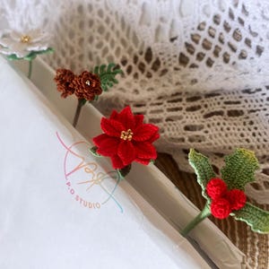 May include: Four crocheted flower and leaf embellishments. The embellishments are red, white, brown, and green. The embellishments are on a white background with a colorful logo that says "P.O. Studio".
