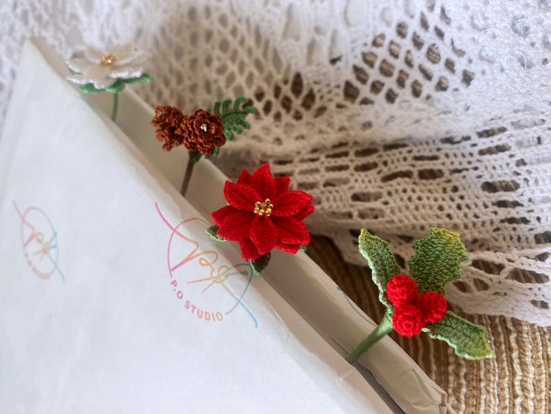 May include: Four crocheted flower and leaf embellishments. The embellishments are red, white, brown, and green. The embellishments are on a white background with a colorful logo that says "P.O. Studio".