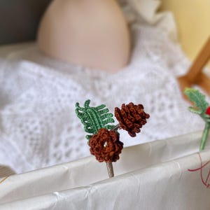 May include: Two crocheted pine cone ornaments with green leaves and a crocheted holly ornament with red berries.