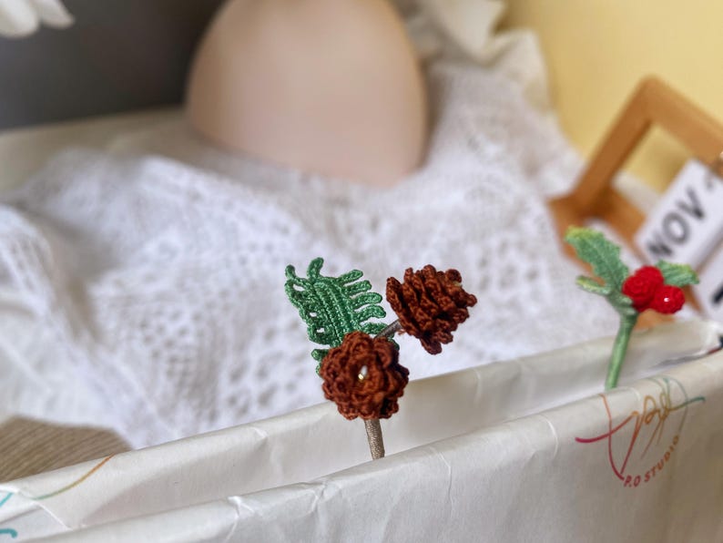 May include: Two crocheted pine cone ornaments with green leaves and a crocheted holly ornament with red berries.