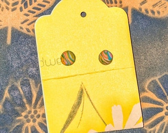 May include: A pair of small, round earrings with a colorful swirl pattern. The earrings are displayed on a yellow card with a hole in the top for hanging.