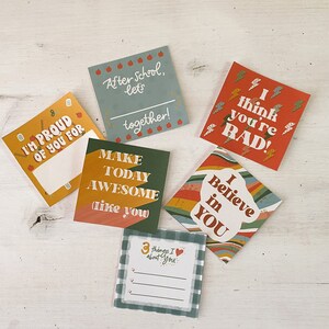 Op de afbeelding: Een verzameling kleurrijke vierkante kaarten met verschillende berichten. E&eacute;n kaart leest "I'M PROUD OF YOU FOR" met ruimte om te schrijven. Andere kaarten zeggen "After school, let's together!", "I think you're RAD!", "Make today awesome like you", "I Believe in YOU" en "3 things I about you".