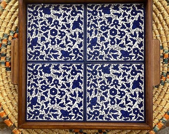 Könnte beinhalten: Ein quadratisches Serviertablett aus Holz mit vier quadratisch angeordneten Keramikfliesen. Jede Fliese zeigt ein sich wiederholendes Muster aus dunkelblauen Blumen, Blättern und Ranken auf weißem Grund. Das Tablett hat einen dunkelbraunen Holzrahmen.