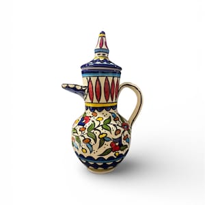 May include: A hand-painted ceramic pitcher with a lid. The pitcher features a cream-colored base adorned with colorful floral and leaf patterns. The lid and base are trimmed with blue, red, and yellow accents. The pitcher has a curved handle and a spout.