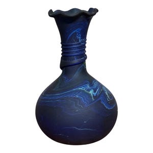 May include: A dark blue glass vase with a bulbous body and a ruffled rim. The vase features a swirling pattern of lighter blue and white, with a wrapped neck detail. Decorative home decor.