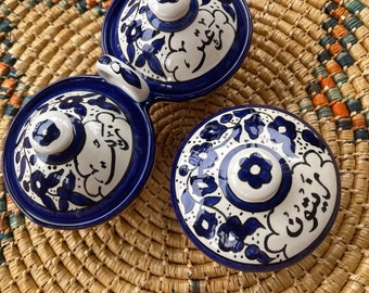 May include: Three blue and white ceramic bowls with intricate floral designs and Arabic script. The bowls are arranged on a woven straw mat.