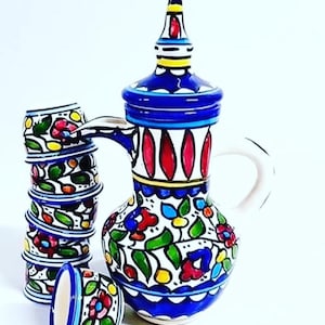 May include: A set of colourful ceramic teacups and a teapot with a floral design. The teapot has a blue and white base with a red and yellow lid. The teacups are stacked and have a similar floral design.