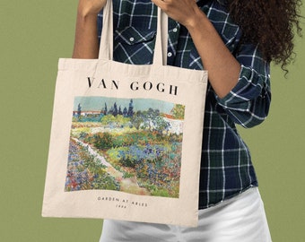 May include: A woman is holding a white tote bag with a painting of a garden by Van Gogh. The painting is titled "Garden at Arles, 1888".