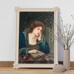 May include: A painting of a woman in a blue dress, sitting in a garden setting, reading a book. She is wearing a floral headband and has her hand resting on the book. The painting is framed in a white frame.