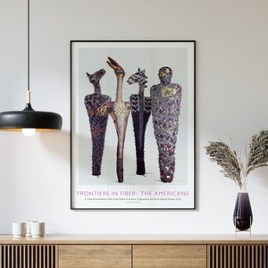 Peut inclure: Une affiche intitulée "Frontiers in Fiber: The Americans" présentant une œuvre d'art abstraite et colorée de quatre figures. Les figures sont faites de divers matériaux, dont du tissu, du bois et du métal. L'affiche est encadrée de noir et est accrochée à un mur blanc au-dessus d'un meuble en bois.