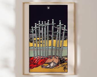 May include: A framed tarot card print featuring the Ten of Swords. The artwork depicts a figure lying face down with ten swords piercing their back. The background shows a dark sky, a yellow horizon, and a red cloth.