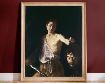 Puede incluir: Una impresión artística enmarcada que representa una figura con una tela clara sobre el hombro, sosteniendo una cabeza cortada por el cabello con una mano y una espada con la otra. La escena presenta un alto contraste sobre fondo oscuro.