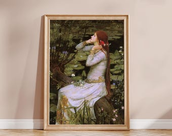 May include: A framed art print depicting a person with long red hair wearing a pale lavender dress with gold trim, seated on a tree trunk near a pond filled with green lily pads and white flowers, set in a light-colored wooden frame.