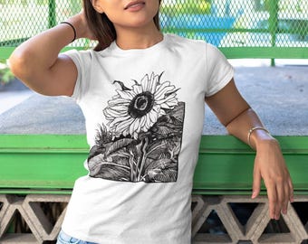 Könnte beinhalten: Ein weißes kurzärmeliges T-Shirt mit einer schwarz-weißen grafischen Illustration einer Sonnenblume mit detaillierten Blättern und Stängeln. Das Motiv ist auf der Brust des T-Shirts zentriert und wird mit einer hellblauen Jeans kombiniert.