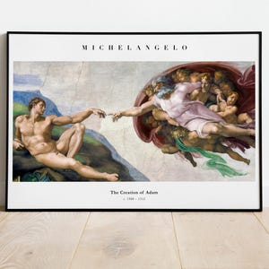 Könnte beinhalten: Ein gerahmter Kunstdruck von Michelangelos Die Erschaffung Adams. Das Gemälde zeigt eine liegende nackte Figur, die nach einer in Gewänder gehüllten Figur umgeben von Putten greift. Oben steht MICHELANGELO, unten The Creation of Adam c. 1508-1512.