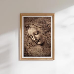 Könnte beinhalten: Ein gerahmter Wandkunstdruck mit einer sepiafarbenen Skizze eines menschlichen Gesichts mit gesenktem Blick und fließendem Haar. Das Kunstwerk ist in einer monochromen braunen Palette mit sichtbaren kohleartigen Strichen gehalten.
