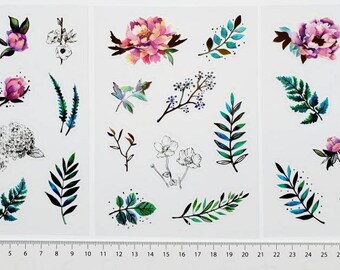 May include: A sheet of floral and botanical stickers featuring watercolor illustrations of flowers, leaves, and branches in shades of pink, purple, green, and blue. Some designs are outlined in black. A ruler is at the bottom.