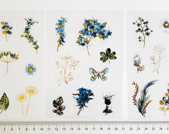 May include: Three sheets of clear sticker paper with blue and gold floral designs. The stickers feature various flowers, leaves, and feathers.