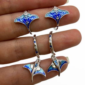 Peut inclure: Ensemble de boucles d'oreilles et de bagues en argent sterling avec un motif de raie manta en émail bleu et turquoise. Les boucles d'oreilles sont de style créole avec un pendentif. Les bagues ont un design similaire.