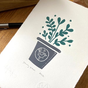 Puede incluir: Una impresión de linóleo en gris y verde de una planta en maceta con un pájaro en un círculo en la maceta. La impresión está firmada "Aizz" y "growing green" en la esquina inferior derecha. La impresión está estampada con un círculo que contiene un pájaro y las letras "C4G".