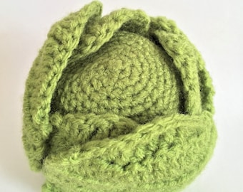 May include: A crocheted green cabbage with a textured surface. The cabbage is made with a green yarn and has a realistic appearance.