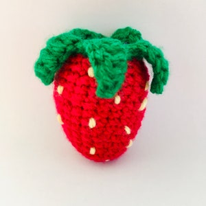 May include: A crocheted strawberry with a red body and green leaves. The strawberry has white stitches that resemble seeds.