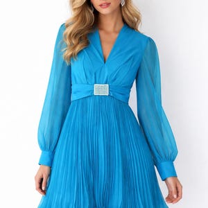 May include: A vibrant turquoise dress with long, sheer sleeves and a pleated skirt. The dress features a V-neckline and a sparkling rectangular buckle at the waist. The skirt has a ruffled hemline.