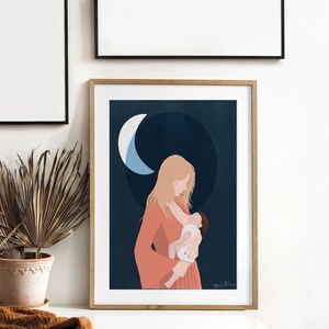 Op de afbeelding: Een ingelijste kunstafdruk toont een moeder die een baby vasthoudt, tegen een donkerblauwe achtergrond met een halve maan. De moeder draagt een koraalkleurige jurk. De print zit in een houten lijst.