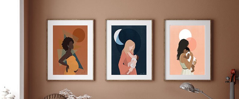 Op de afbeelding: Drie ingelijste kunstdrukken over het thema moederschap. De eerste prent toont een zwangere persoon in een gele jurk tegen een oranje achtergrond. De tweede toont een persoon die een baby vasthoudt onder een halve maan. De derde toont een persoon die een baby vasthoudt.