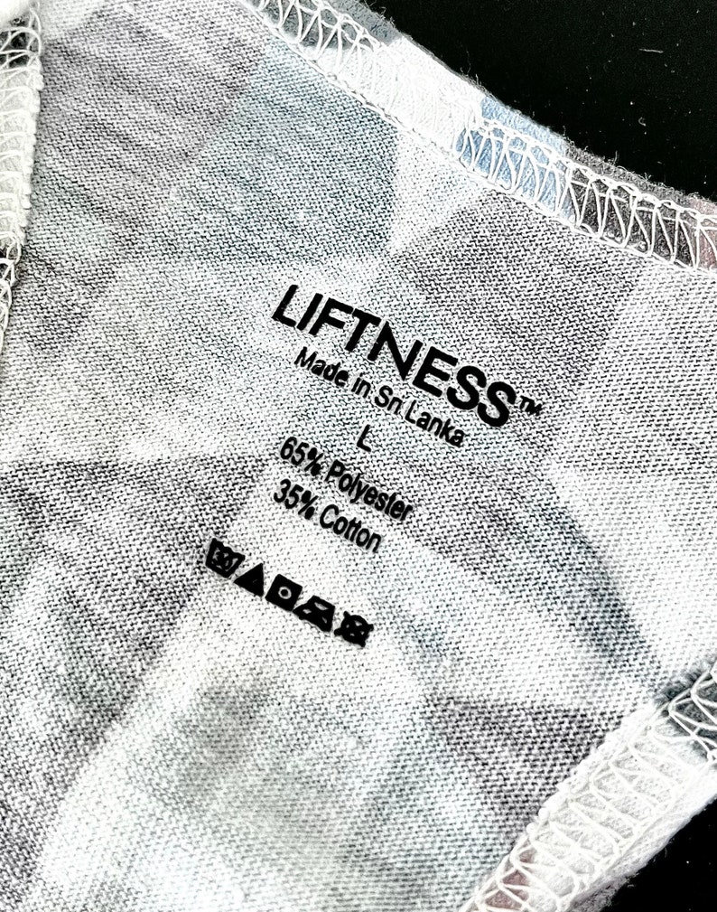 May include: A white tag with black text that reads "LIFFTNESS&trade; Made in Sri Lanka L 65% Polyester 35% Cotton" and a set of care instructions symbols.