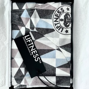 May include: A black and white geometric patterned fabric with a blue and gray geometric pattern. The fabric is in a black box with a black tag that says "Liftness TM Designed in London, UK".