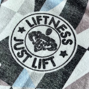 May include: A white and gray patterned fabric with a black circle containing the text "Just Lift Fitness" and a stylized image of a person lifting weights.