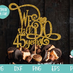 May include: Gold glitter cake topper with the text "We're still 45 years" and a heart. The topper is on top of a chocolate cake with chocolate chips and other decorations.