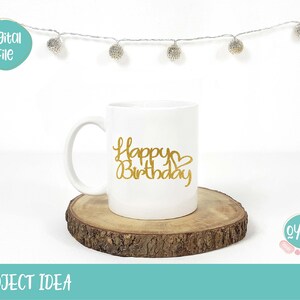 Op de afbeelding: Een witte keramische mok met een gouden glitterontwerp met de tekst "Happy Birthday" met een hartje. De mok staat op een houten schijf.