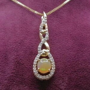 Könnte beinhalten: Eine goldfarbene Halskette mit Anhänger, die einen ovalen, hellfarbigen Edelstein umgeben von kleinen, klaren Steinen zeigt. Der Anhänger hat ein aufwendiges Design mit einer filigranen Kette, präsentiert auf einer lila Samtbüste.