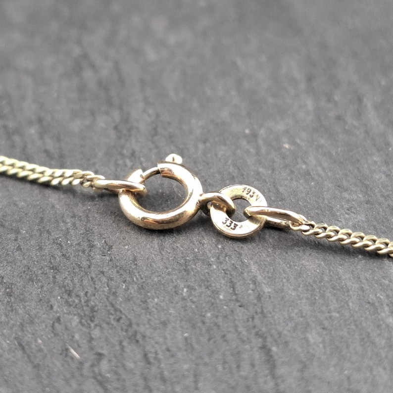 May include: A gold-toned metal chain necklace featuring a circular spring ring clasp. A small circular tag attached to the clasp is engraved with the text 333 and 193V, indicating the metal purity and identification marks on the jewelry piece.