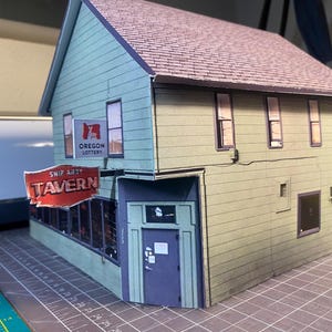 May include: A miniature model of a two-story building with a light green exterior and a brown roof. The sign reads "Ship Ahoy Tavern" in red and white. The building also has an "Oregon Lottery" sign.