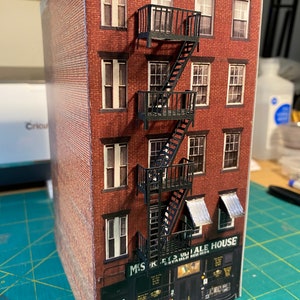 Op de afbeelding: Een model van een bakstenen gebouw met een brandtrap en een bord met de tekst "Mickey's Ale House Established 1854".