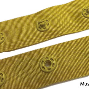 May include: Close-up of yellow fabric with a row of yellow plastic snap buttons. The fabric has a woven texture. The text "Mustard" is visible at the bottom of the image.