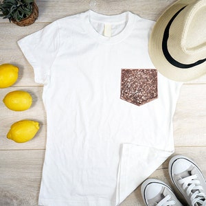 May include: White t-shirt with a sparkly pink pocket and a pair of white sneakers. There is a straw hat and lemons on a wood background.
