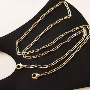 May include: Gold chain mask strap with two lobster clasps. The chain is made of linked oval shapes.