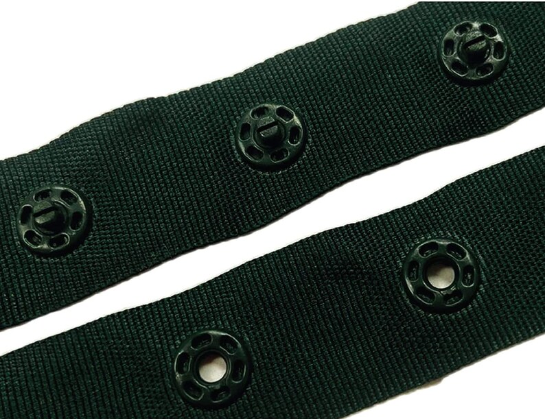May include: Close-up of dark green fabric with black plastic buttons. The fabric has a woven texture and the buttons have a raised ring around the centre hole.