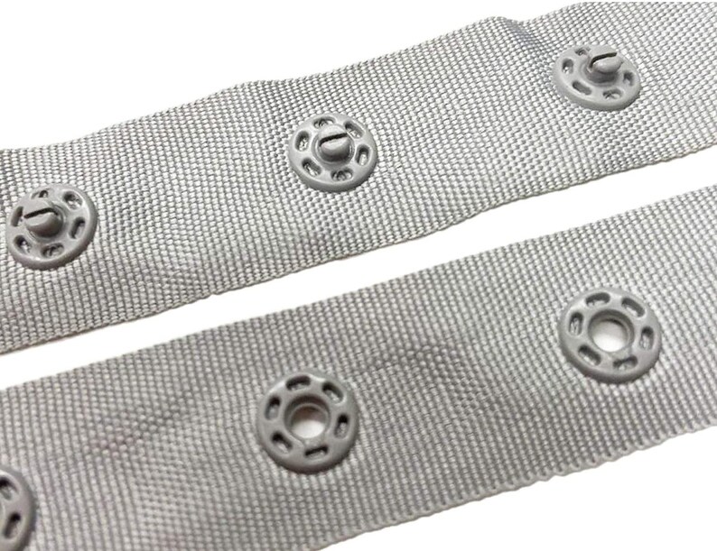 May include: Grey fabric tape with silver metal eyelets. The tape is designed for use with curtains or other home decor projects.